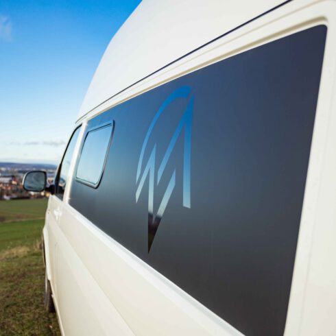 Das Vanlifemanufaktur Logo auf einem VW T6 Campervan mit der Stadt Erfurt im Hintergrund